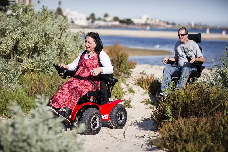 Two people using power wheelchairs to explore a beach