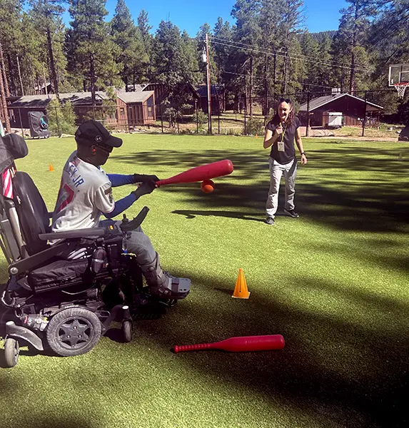 A man using a power wheelchair and hitting a ball with a bat